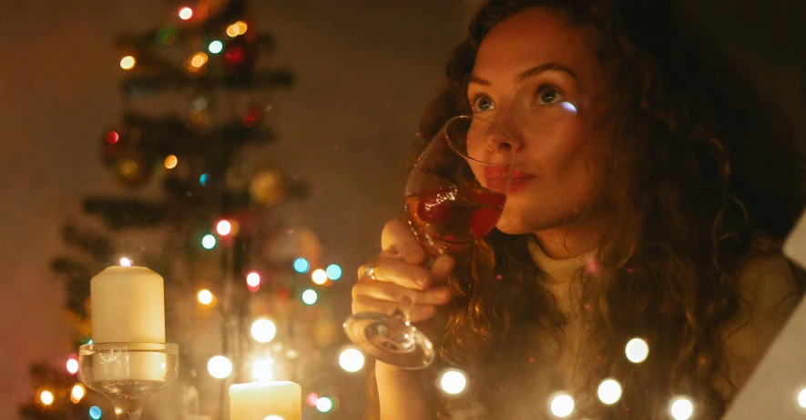 a woman holding a glass of wine in front of a christmas tree, pexels, renaissance, cinematic still, advert, barely lit warm violet red light, drinking whiskey