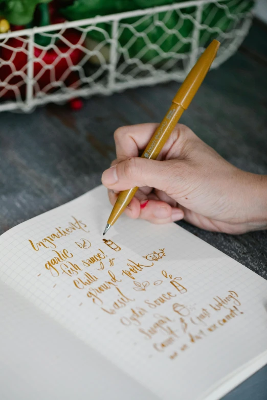 a person writing on a piece of paper with a pencil, gold foil, recipe, thumbnail