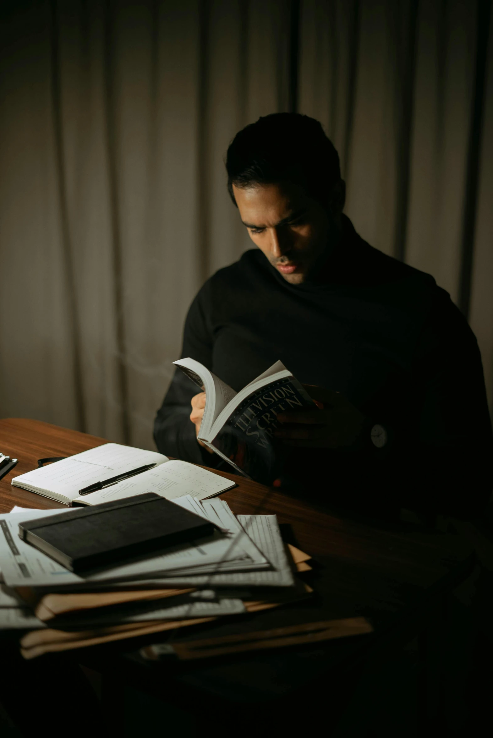 a man sitting at a table reading a book, a portrait, by Pablo Rey, pexels contest winner, vantablack chiaroscuro, holding books, programming, looking serious