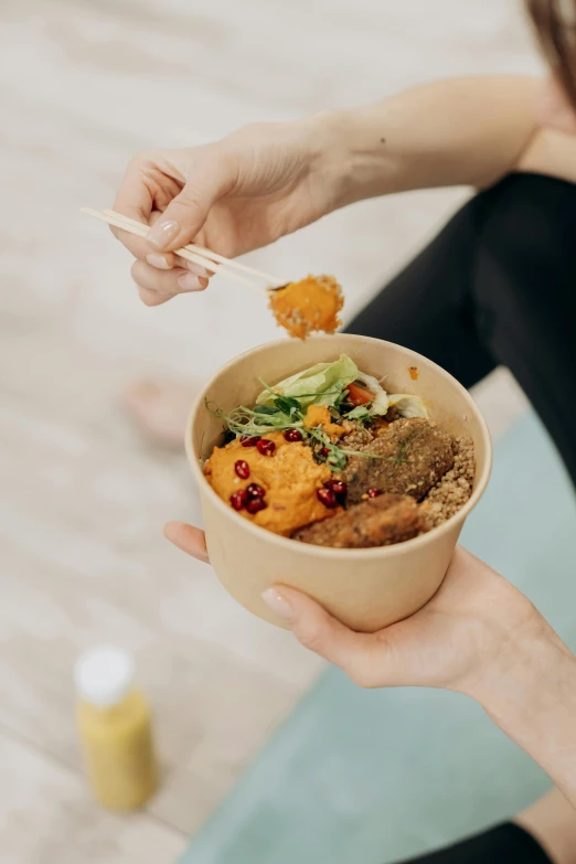 a woman sitting on a yoga mat holding a bowl of food, stick and poke, serving suggestion, professional photo, square