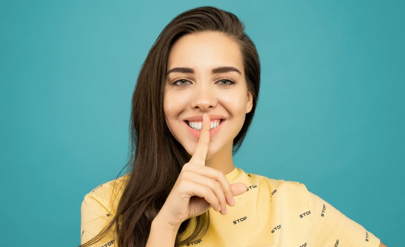 a woman holding her finger to her lips, a colorized photo, shutterstock, antipodeans, cute teeth, avatar image, instagram post, relaxed. blue background