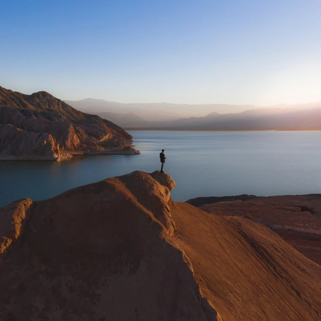 a person standing on top of a mountain next to a body of water, by Daren Bader, pexels contest winner, mexican desert, muted colours 8 k, drone footage, mid morning lighting