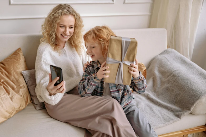 a woman and a child are sitting on a couch, pexels contest winner, holding a very advance phone, holding gift, avatar image, a blond