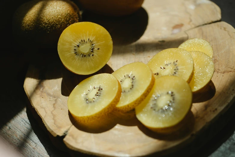 a sliced kiwi sitting on top of a wooden cutting board, by Kristin Nelson, trending on unsplash, hurufiyya, colors: yellow, plates of fruit, golden glistening, thumbnail