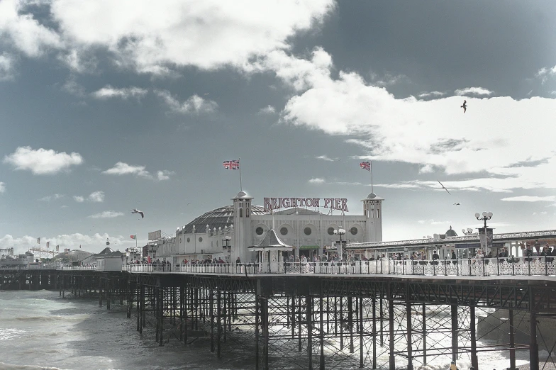 a pier sitting next to the ocean under a cloudy sky, by Nick Fudge, pexels contest winner, seaside victorian building, 🦩🪐🐞👩🏻🦳, classic cinema, slight haze