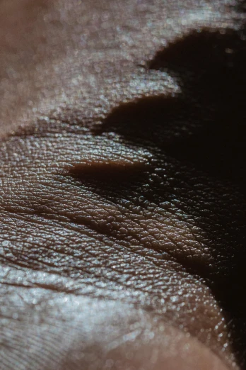 a close up of a piece of leather, inspired by Lucio Fontana, trending on pexels, hyperrealism, hand on her chin, dark brown skin, smooth bioluminescent skin, sweat drops
