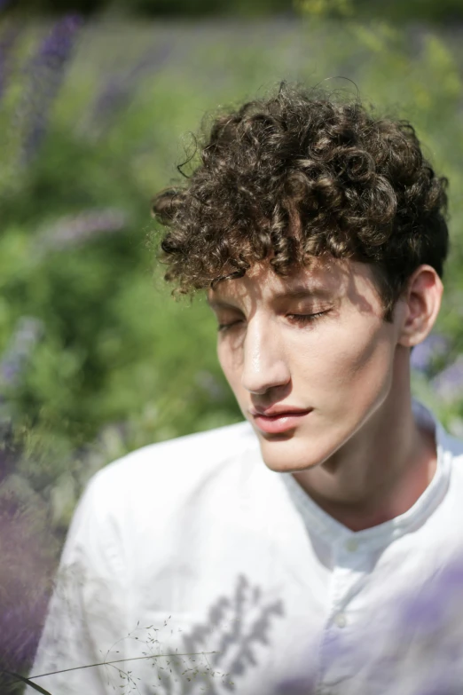 a man standing in a field of purple flowers, an album cover, inspired by John Luke, trending on pexels, renaissance, curly middle part haircut, attractive androgynous humanoid, model photograph, curls