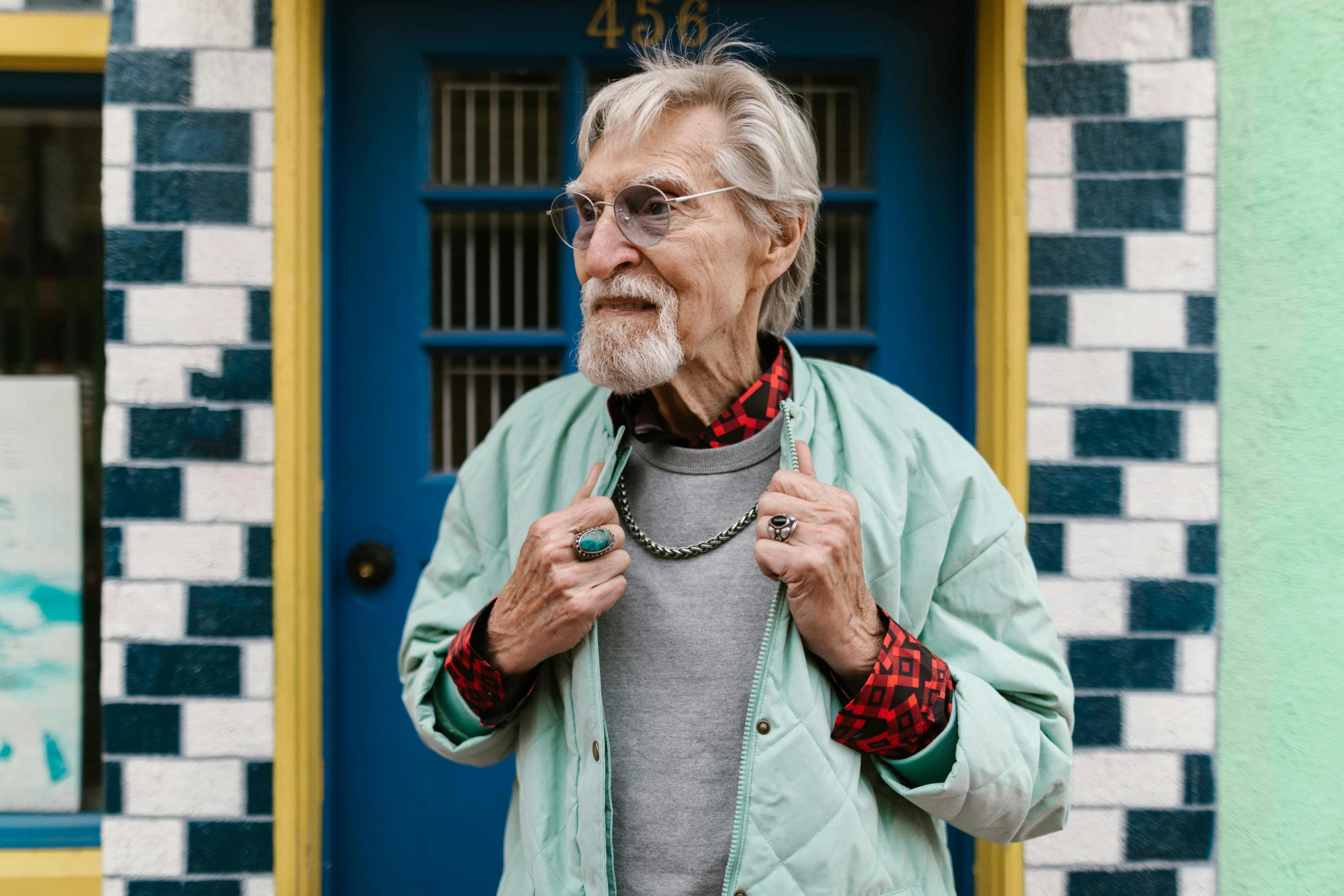 a man standing in front of a blue door, an album cover, by Peter Churcher, pexels, photorealism, gray hair and beard, old lady, eugene gottsnake, multicolored