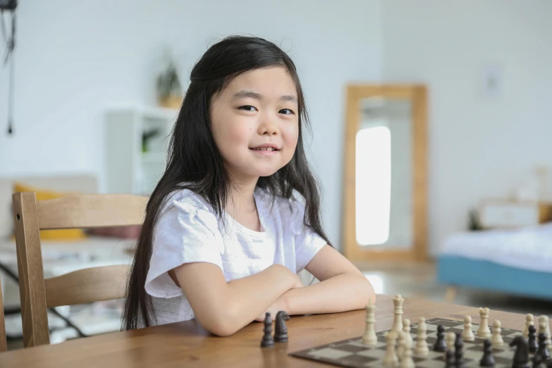 a little girl sitting at a table playing chess, pexels contest winner, american barbizon school, greta thunberg smiling, asian female, youtube thumbnail, girl with warship parts