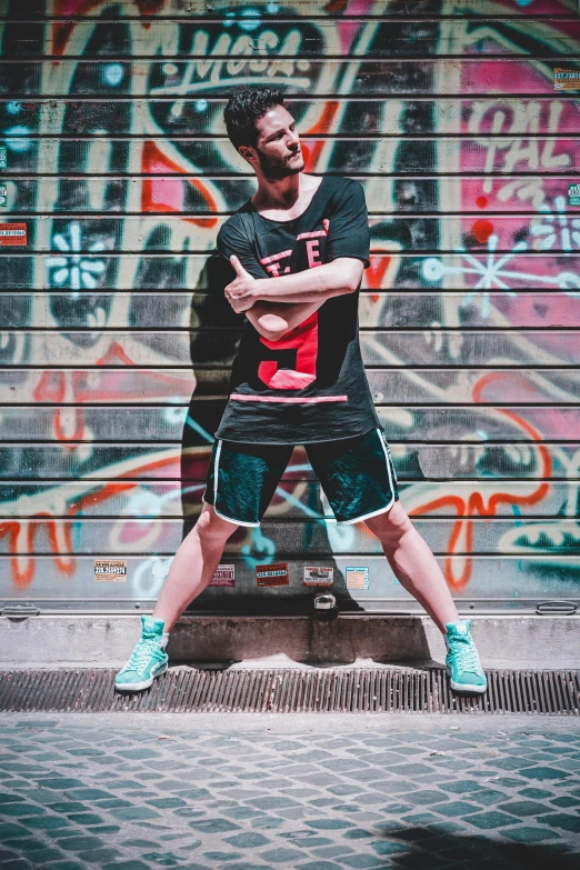 a man standing in front of a graffiti covered wall, pexels contest winner, wearing shorts and t shirt, classic dancer striking a pose, avatar image, sneaker photo