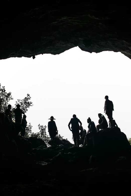 a group of people standing inside of a cave, as seen from the canopy, silhouette :7, large overhangs, carson ellis