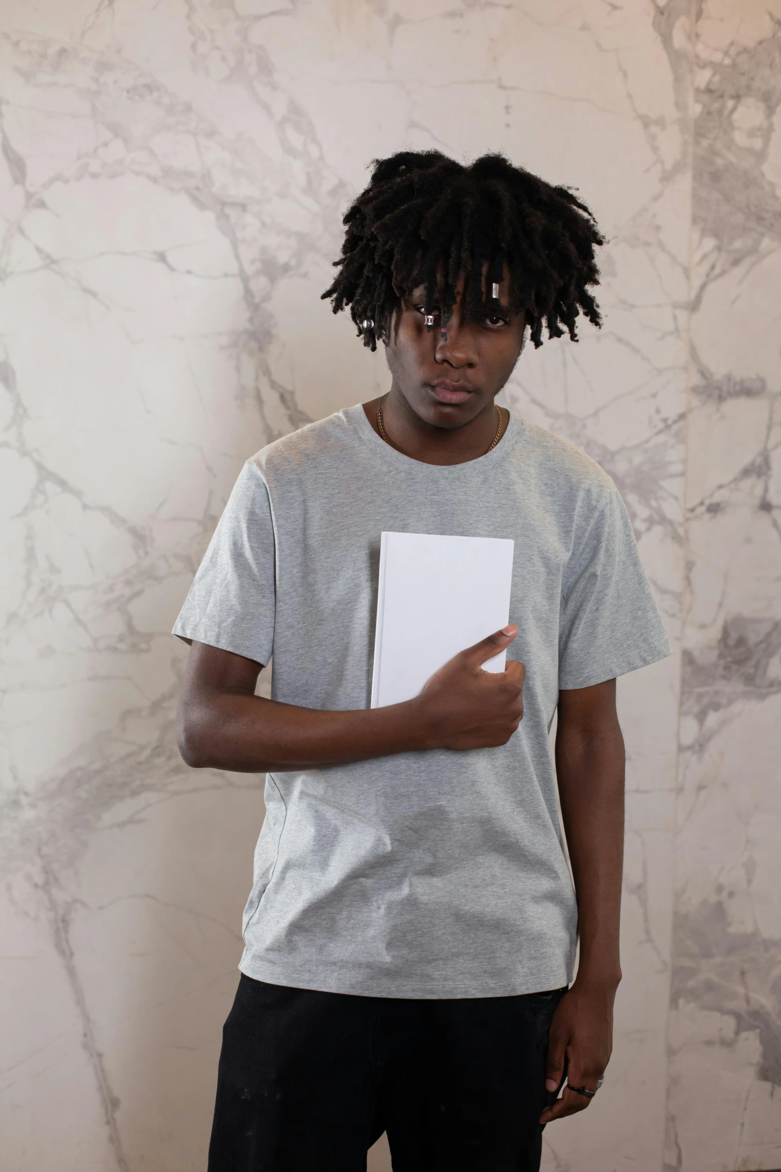 a man standing in front of a wall holding a book, inspired by Xanthus Russell Smith, chief keef, portrait of depressed teen, gray shirt, holding notebook