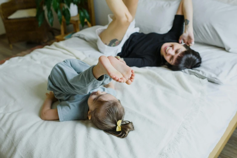 a woman laying on top of a bed next to a baby, pexels contest winner, spinning hands and feet, laying on their back, with a kid, growth of a couple