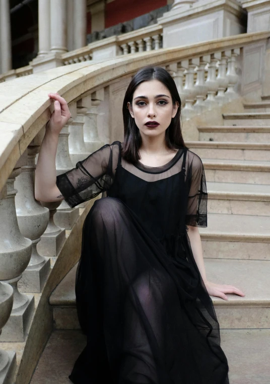 a woman in a black dress sitting on a set of stairs, inspired by Adrienn Henczné Deák, pexels contest winner, renaissance, dark lipstick, see through dress, alexandria ocasio-cortez, melanie martinez