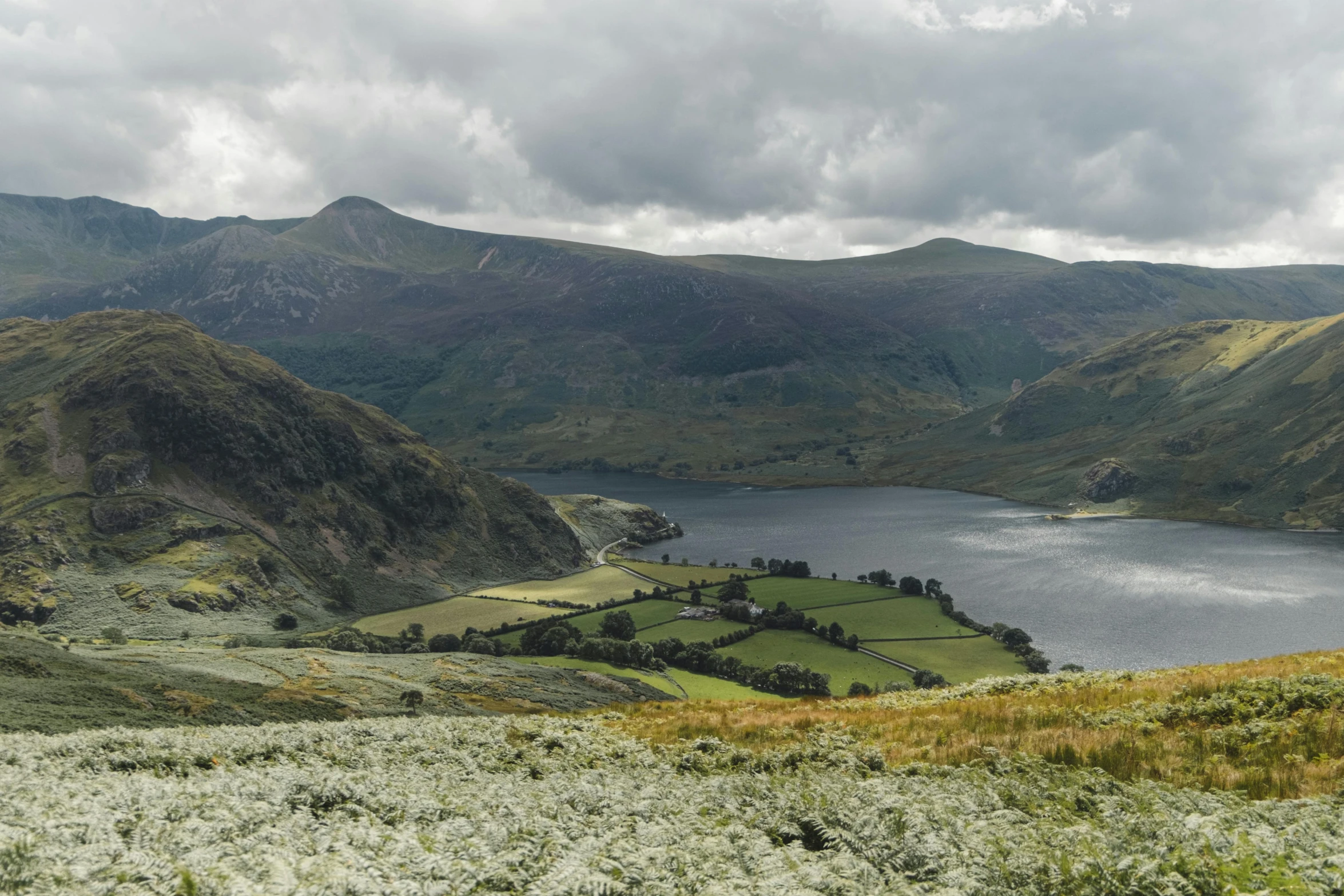 a large body of water sitting on top of a lush green hillside, by Bedwyr Williams, pexels contest winner, hurufiyya, mountains and lakes, slate, regency-era, beach is between the two valleys