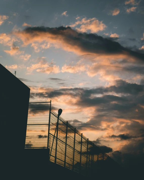 a fence that is next to a building, inspired by Elsa Bleda, pexels contest winner, happening, sunset with cloudy skies, up there, lo-fi, low quality photo