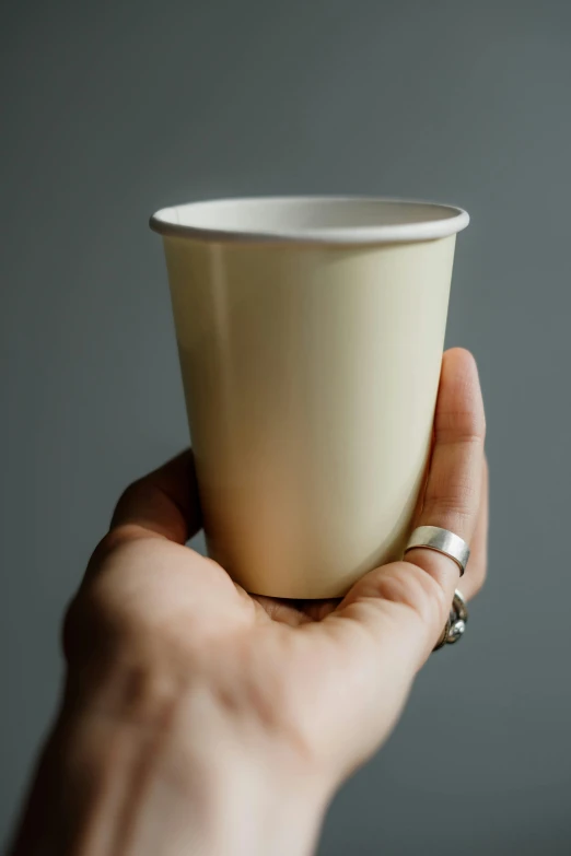 a person holding a cup in their hand, cream paper, professionally assembled, natural soft rim light, yellow tint