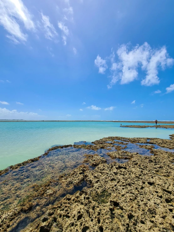 a large body of water sitting on top of a sandy beach, corals, rock pools, clear blue skies, exploration