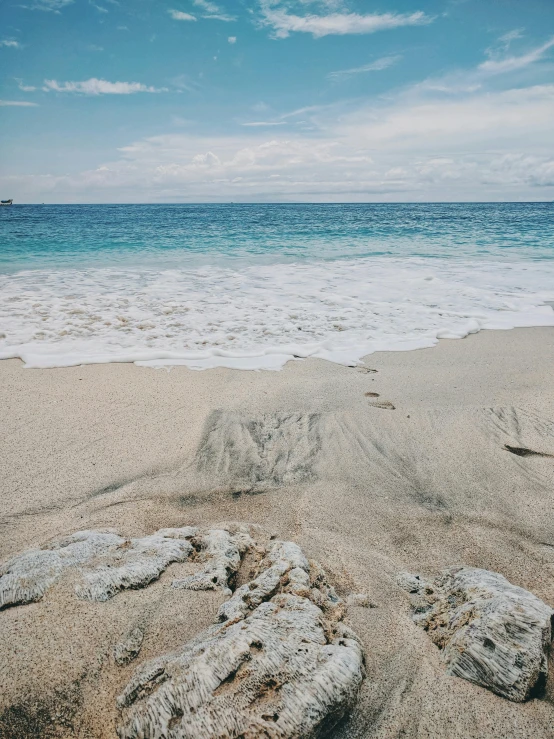 a couple of rocks sitting on top of a sandy beach, the ocean