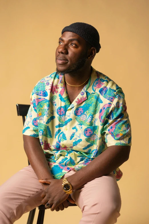 a man in a colorful shirt sitting on a chair, an album cover, inspired by Theo Constanté, trending on pexels, hawaiian shirt, ( ( dark skin ) ), looking away, wearing polo shirt