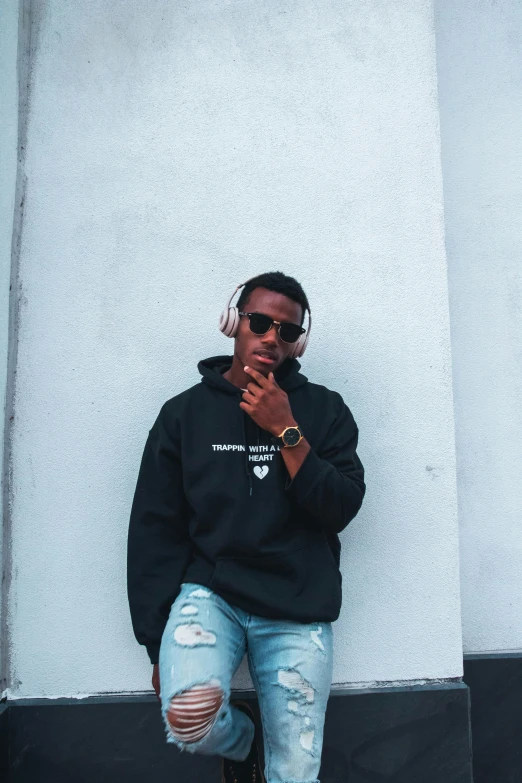 a man sitting against a wall smoking a cigarette, an album cover, trending on unsplash, black hoodie, ( ( dark skin ) ), real trending on instagram image, with sunglasses
