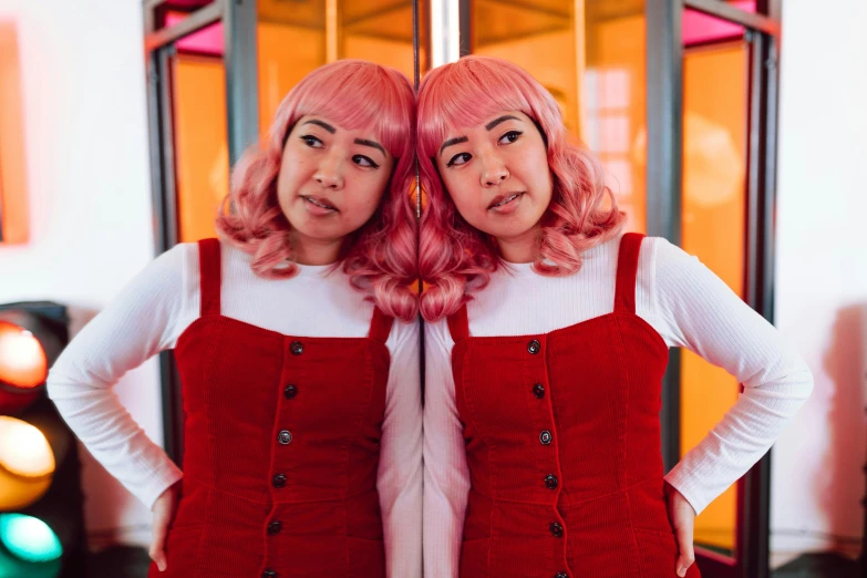 two women standing next to each other in front of a mirror, an album cover, by Julia Pishtar, trending on pexels, red wig, half asian, artist wearing overalls, pink and red color style