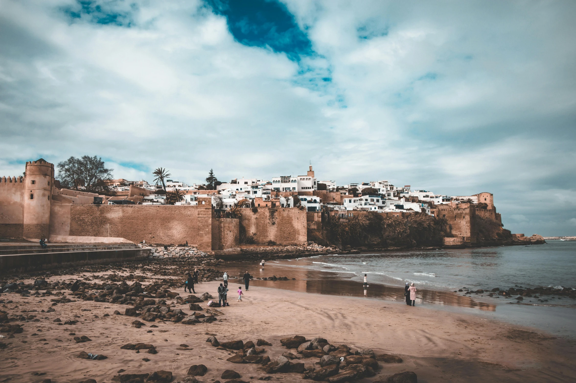 a group of people standing on top of a sandy beach, moorish architecture, villages castles, profile image