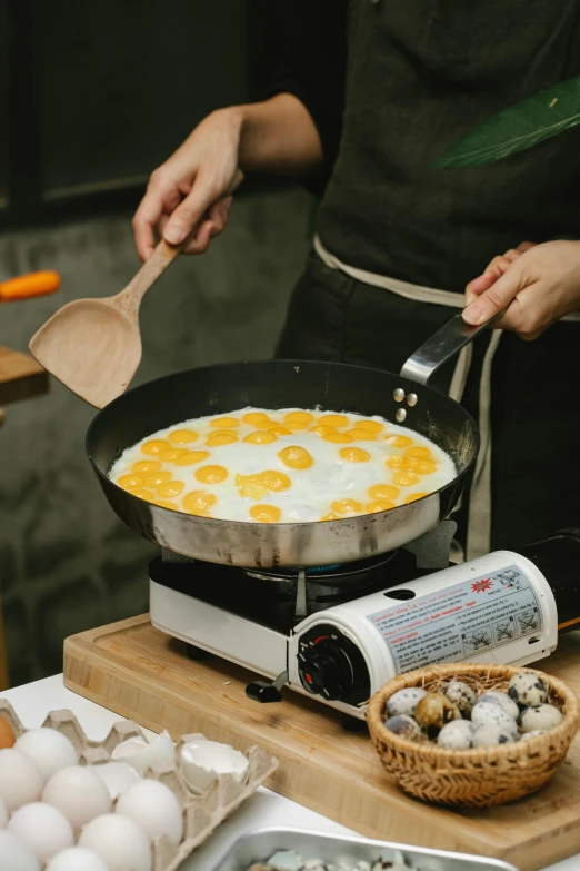 a person cooking eggs in a pan on a stove, 王琛, on a wooden tray, tall, fully covered