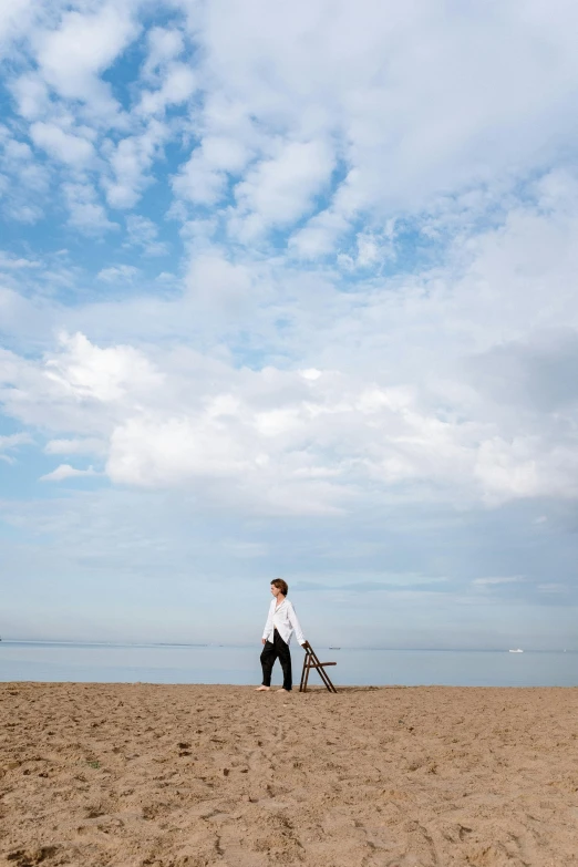 a man standing on top of a sandy beach, inspired by Storm Thorgerson, unsplash, minimalism, late summer evening, carrying a tray, chicago, easel