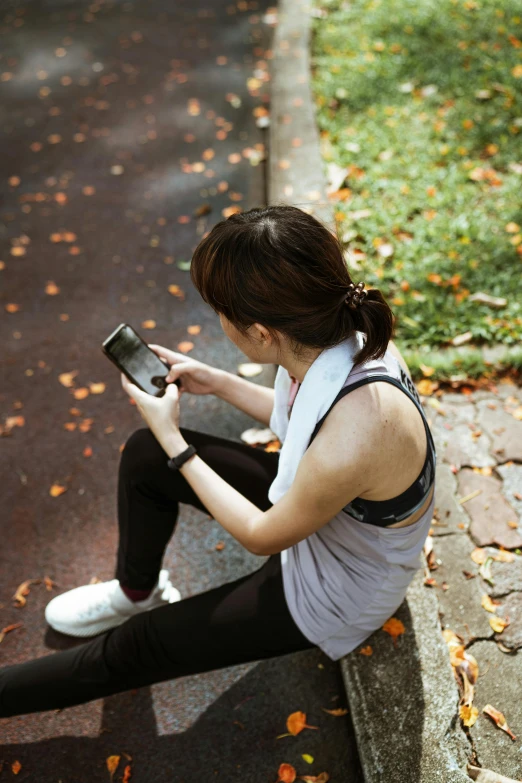 a woman sitting on a curb using a cell phone, wearing fitness gear, sitting on a leaf, deteriorated, square