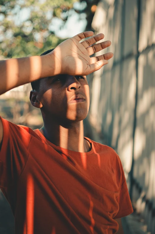 a man standing in front of a building with his hands on his head, pexels contest winner, sunlight filtering through skin, black teenage boy, closeup of sweating forehead, orange hue