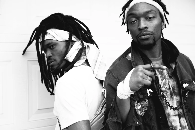 a couple of men standing next to each other, an album cover, short dreadlocks with beads, black and white picture, hip-hop, looking off to the side