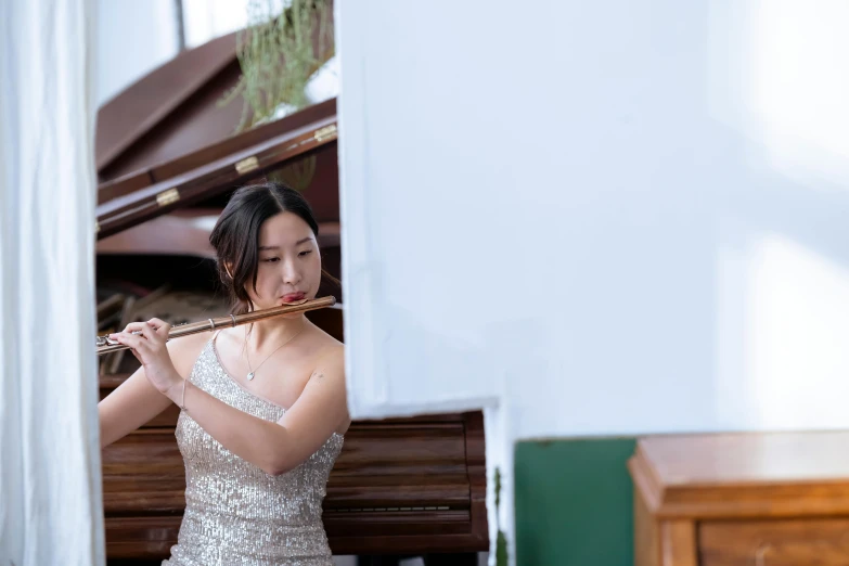 a woman playing a flute in front of a piano, inspired by Zheng Xie, unsplash, wearing an elegant dress, in front of white back drop, on the altar, a young asian woman