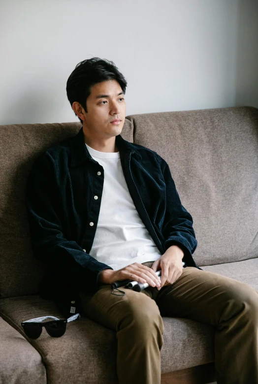 a man sitting on top of a couch next to a window, inspired by Joong Keun Lee, unsplash, a handsome man，black short hair, wearing jacket, promo image, on a couch