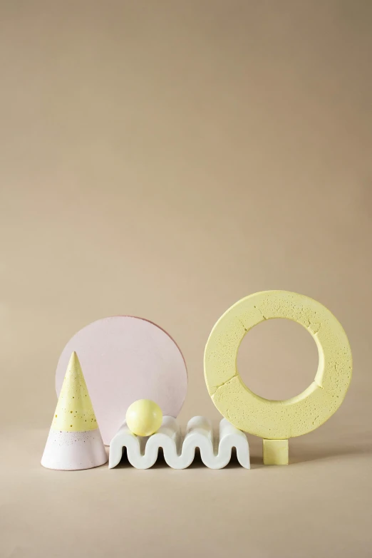 a couple of letters sitting on top of a table, an abstract sculpture, inspired by Isamu Noguchi, trending on behance, new sculpture, pink and yellow, ice cream cone, various sizes, single object scene