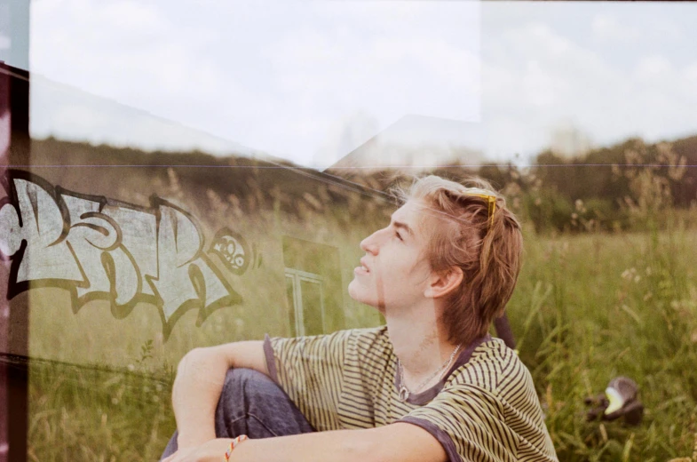 a woman sitting in the grass in front of a bus, a picture, inspired by Caspar Wolf, unsplash, graffiti, beautiful boy, side portrait of imogen poots, looking outside, overexposed photograph