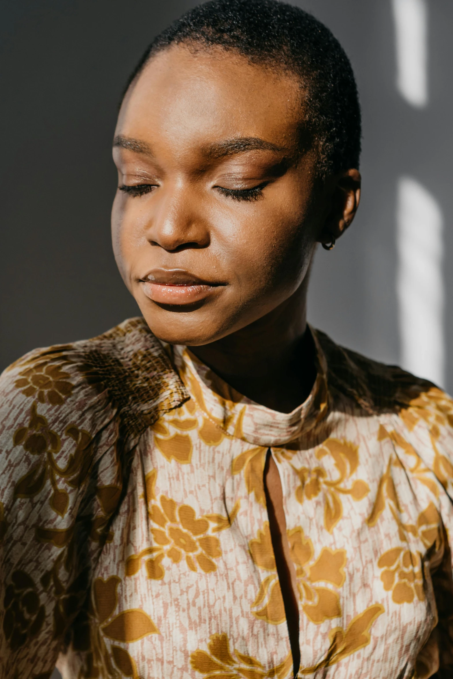 a woman standing in front of a window with her eyes closed, trending on unsplash, wearing yellow floral blouse, portrait of ororo munroe, cheekbones, muted brown