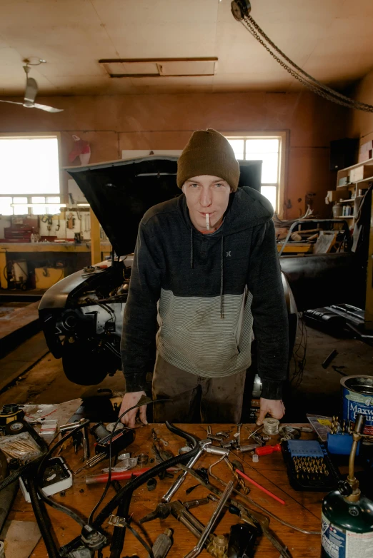 a man standing in front of a table full of tools, aussie, man wearing a closed cowl, exposed mechanics, profile image