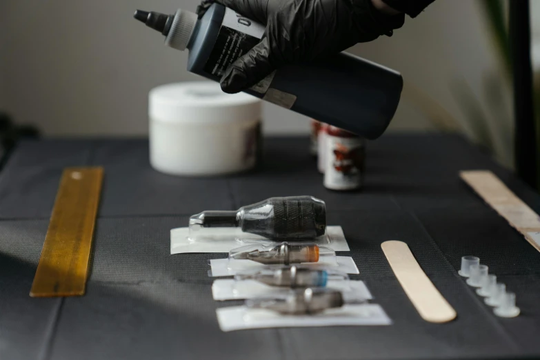 a person using a nail dryer on a table, a hyperrealistic painting, by Ben Zoeller, pexels contest winner, hyperrealism, small vials and pouches on belt, tattoo ink, ingredients on the table, black ink