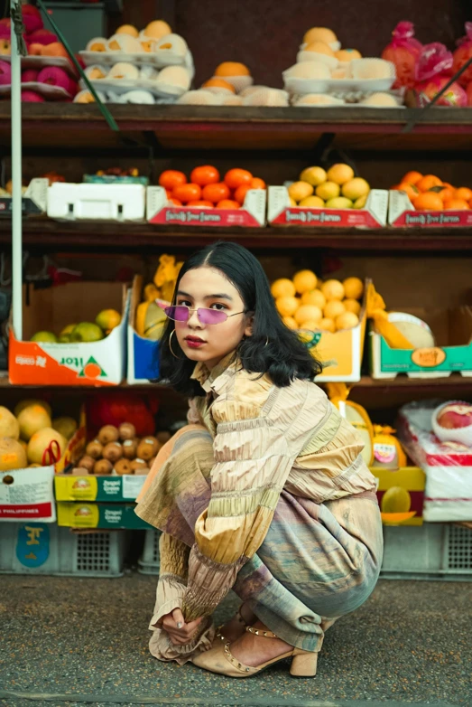 a woman sitting on the ground in front of a fruit stand, an album cover, inspired by Elsa Bleda, trending on pexels, wavy long black hair and glasses, model wears a puffer jacket, asian male, stood in a supermarket