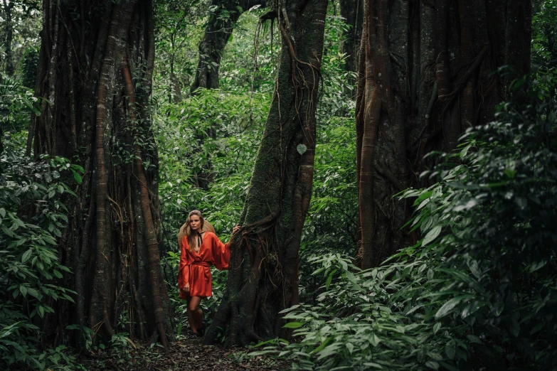 a woman standing in the middle of a forest, inspired by Steve McCurry, sumatraism, orange robe, in jungle, lachlan bailey, person made of tree