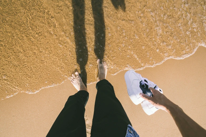 a man standing on top of a sandy beach next to the ocean, a picture, unsplash, realism, wearing white sneakers, long cast shadows, detailed shot legs-up, partially submerged