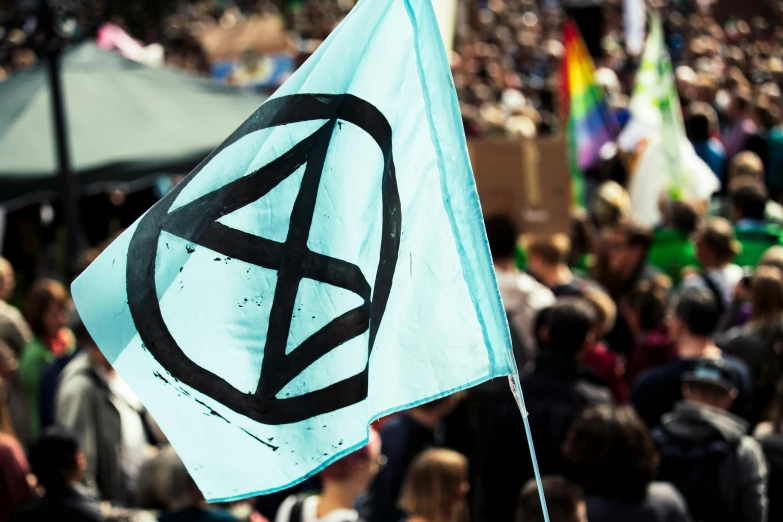 a large group of people standing around a blue flag, unsplash, antipodeans, crass records, square, eco, x logo