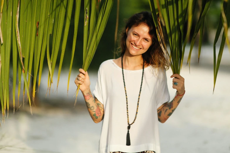 a woman standing under a palm tree on the beach, a portrait, by Caroline Mytinger, pexels contest winner, hurufiyya, wearing shipibo tattoos, avatar image, smiling at camera, bone jewellery