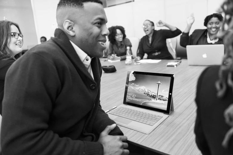 a group of people sitting around a table with laptops, a black and white photo, by Marshall Arisman, happening, brown skin man with a giant grin, sharp focus on scenery, microsoft, j. h. williams iii