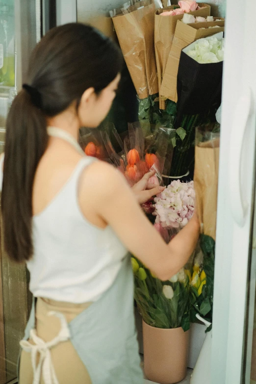 a woman standing in front of a refrigerator holding a bunch of flowers, pexels, shop front, opening, cardboard, mai anh tran