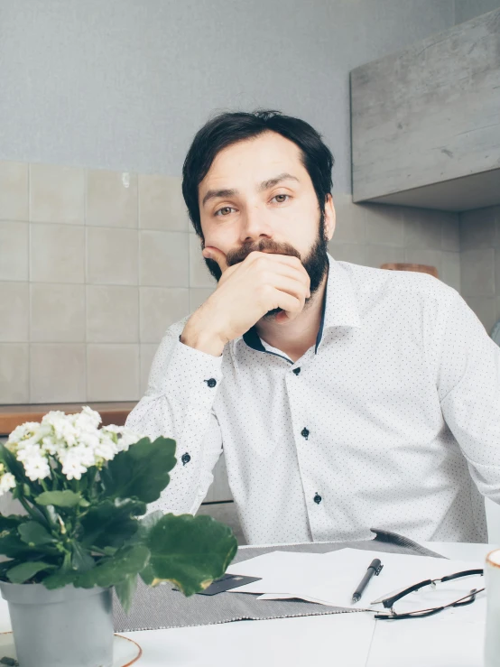 a man sitting at a table with a cup of coffee, inspired by Illarion Pryanishnikov, pexels contest winner, romanticism, beard stubble, sitting with flowers, in a kitchen, wearing a shirt with a tie