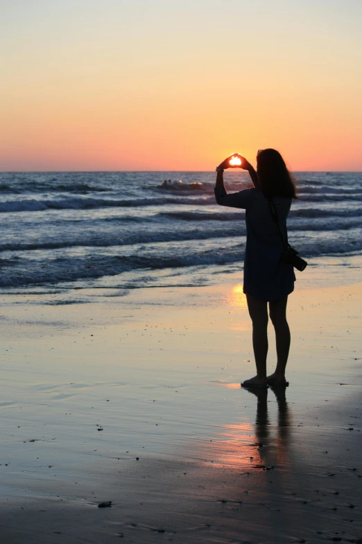 a woman standing on top of a beach next to the ocean, hearts, which shows a beach at sunset, oceanside, university