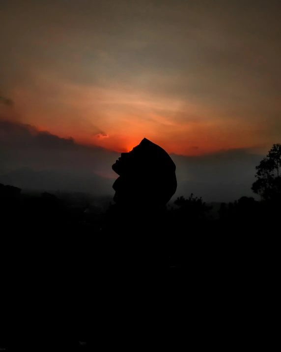 a person standing on top of a hill at sunset, by Emma Andijewska, sumatraism, giant head statue ruins, profile image, dark photo, hanuman!! head building