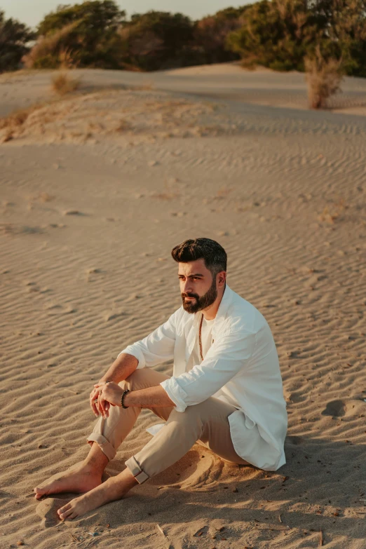 a man sitting on top of a sandy beach, an album cover, inspired by Amir Zand, pexels contest winner, renaissance, wearing a white button up shirt, bearded beautiful man, desert colors, middle east